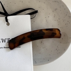 Detailed close-up of a tortoiseshell acetate hair clip with a minimalist jewelry tag
