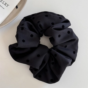 Detail of black fabric scrunchie with textured 3D polka dots on a minimalist white setup