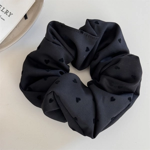 Close-up of black scrunchie with heart pattern and soft fabric texture on white background