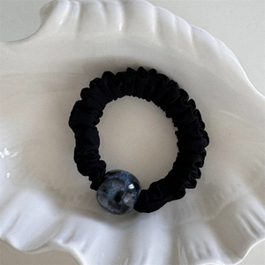 Dettaglio di un elastico per capelli nero a pieghe con una perla di resina marmorizzata