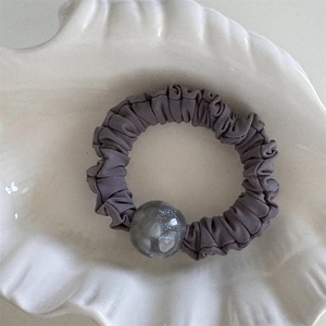 Dettaglio dell'elastico per capelli a pieghe grigio scuro con una grande perla decorativa