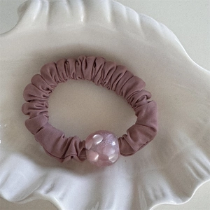 Dettaglio di elastico per capelli a pieghe color malva con perla glitterata in ciotola