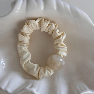 Dettaglio scrunchie color crema a pieghe con grande perla perlata in un vassoio a conchiglia