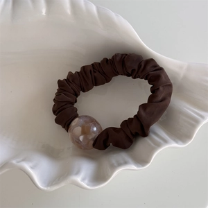 Dettaglio di un elastico per capelli marrone con perla d'ambra in un piatto a conchiglia