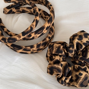 Detail of leopard print padded headband and matching scrunchie on white fabric texture