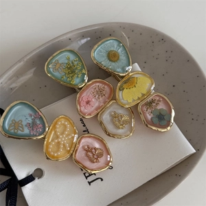 Detailed macro view of resin hair clips with dried flowers and pearl butterfly motifs