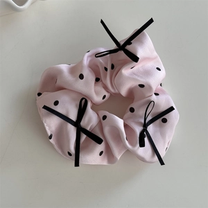 Vista dettagliata dello scrunchie rosa a pois con fiocchi di nastro nero e trama satinata