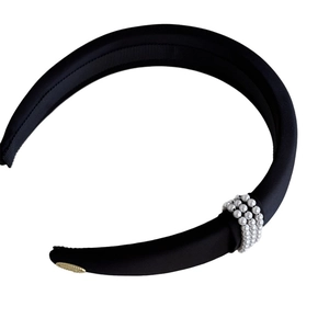Elegant black satin padded headband with pearl accents and gold logo charm on white background