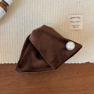 Close-up of a brown velvet hair clip with a large pearl on a rustic textured background