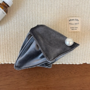Detailed view of dark grey velvet hair claw with a large pearl on a woven mat