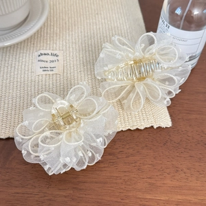 Detail of two white bubble gauze flower hair claws with elegant polka dot mesh texture