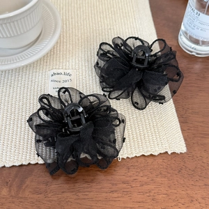 Close-up of two black mesh flower hair claws on a woven mat with aesthetic props