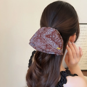 Brown paisley floral scrunchie for women with gold logo tag shown on a low ponytail