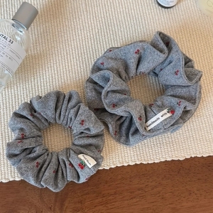 Elegant grey knitted scrunchies with cherry print and handmade label on a textured mat