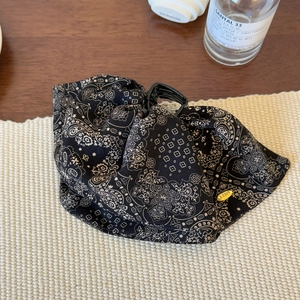 Detail of a black paisley print hair claw clip with a gold metal tag on a textured mat