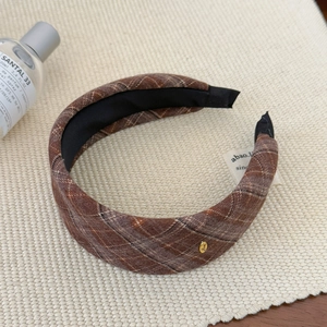 Brown plaid wide headband with gold metal Love charm on woven textured background
