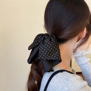 Rear view of a model wearing a black polka dot bow hair scrunchie on a ponytail