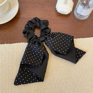 Detail of black satin scrunchie with white polka dot ribbon on a woven mat