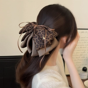 Close-up of leopard print bow hair clip with vintage silk ribbons and metal brand tag