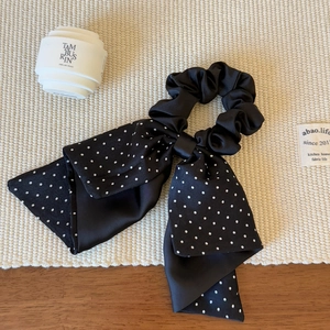 Detail of black satin bow scrunchie with white polka dots on a natural wood surface