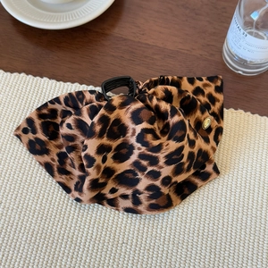 Detailed close-up of a leopard print fabric bow hair claw with a gold metal emblem
