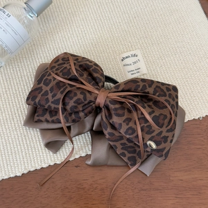 Detail of leopard print bow hair clip with satin ribbon and gold metal tag