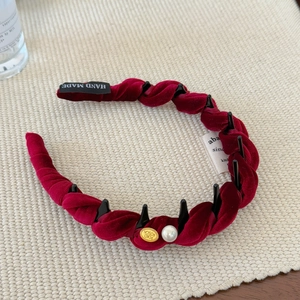 Détail du serre-tête tressé en velours bordeaux avec perle et emblème en métal doré