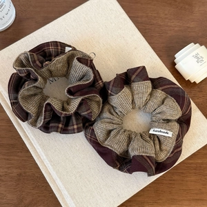 Detailed close-up of brown and burgundy plaid hair scrunchies with handmade cloth label