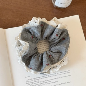 Detailed shot of grey knit scrunchie with lace edges and cherry embroidery on an open book