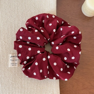 Close-up of a burgundy red polka dot satin scrunchie on a woven mat with a candle