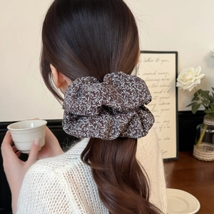 Detailed view of a dark brown floral scrunchie styled in a French retro aesthetic