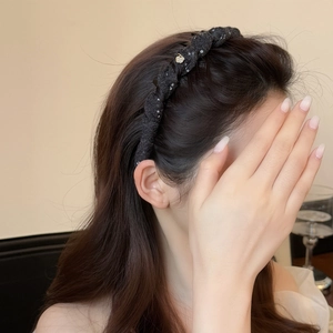 Elegant twisted black headband with sparkly texture and gold heart detail on a model