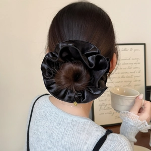 Gros plan sur un chouchou oversize en satin noir sur un chignon avec breloque dorée