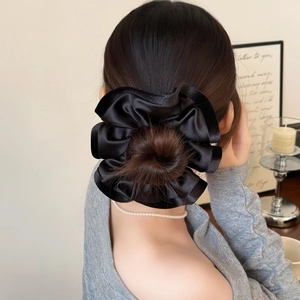 Chouchou élégant en satin noir à volants plissés porté sur un chignon de cheveux