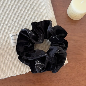 Close-up of black velvet scrunchie featuring silver glittery bow patterns and soft texture