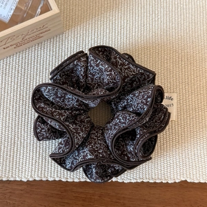 Close-up of vintage brown floral scrunchie with .life logo tag on rustic wooden background