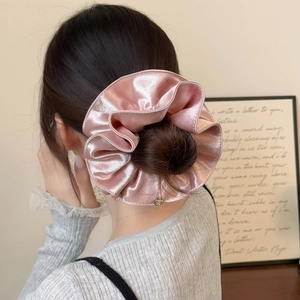 Vue détaillée du chouchou en satin rose champagne avec texture brillante et breloque dorée