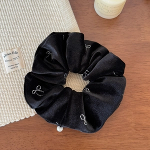 Detail of black velvet scrunchie with silver bow print and white pearl charm detail
