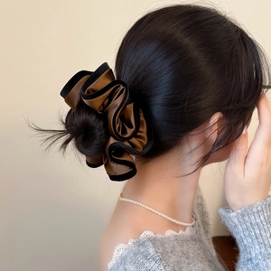 Détail d'un grand chouchou en satin bronze avec bordure en velours noir sur un chignon