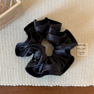 Gros plan d'un chouchou en satin noir avec bordure en velours sur fond texturé