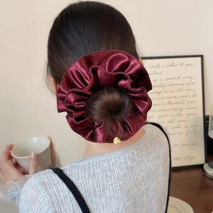 Vue détaillée d'un chouchou en satin bordeaux luxueux avec un petit pendentif doré