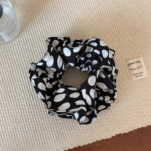 Gros plan d'un chouchou en satin à pois noirs et blancs sur un fond de texture tissée