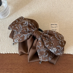 Détail d'une pince à cheveux avec nœud en satin marron, motifs floraux et perles