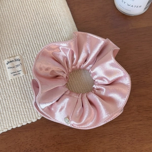Détail du chouchou en satin rose avec texture de soie douce et breloque en métal