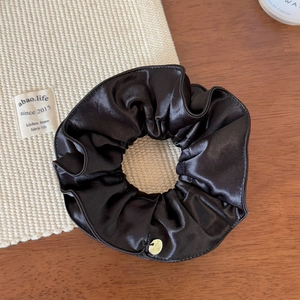 Gros plan détaillé du chouchou en satin foncé avec texture brillante et pendentif doré