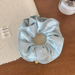 Détail du chouchou en satin bleu clair avec un petit pendentif doré élégant
