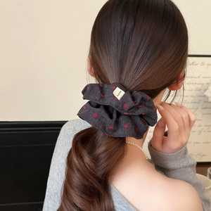 Detail of red polka dot denim scrunchie with Hand Made tag worn on a ponytail