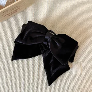 Detail of a large black velvet bow hair clip on textured beige fabric background