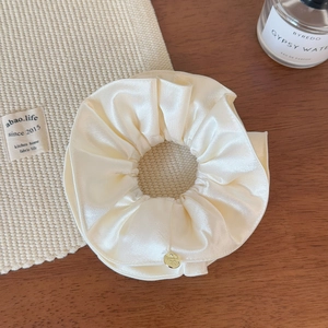 Gros plan sur un chouchou en satin crème avec texture soyeuse et détail doré chic