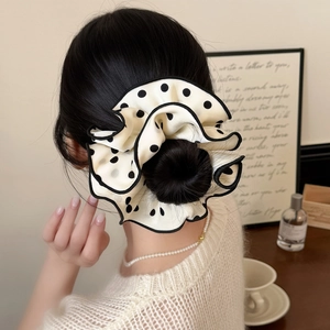 Elegant cream polka dot scrunchie with black trim on a messy bun hairstyle